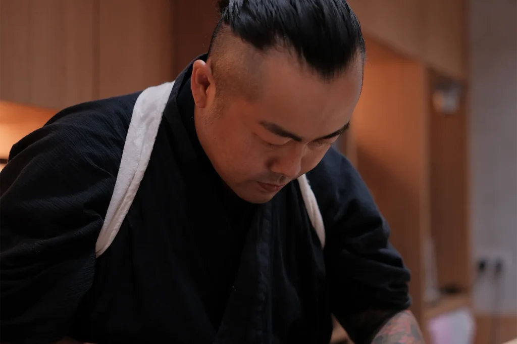 Profile shot of a professional sushi chef with a top-knot hairstyle focused on preparing an omakase meal.