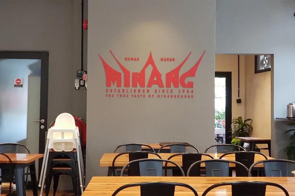 The modern interior of Rumah Makan Minang restaurant showing the logo and wooden dining tables.
