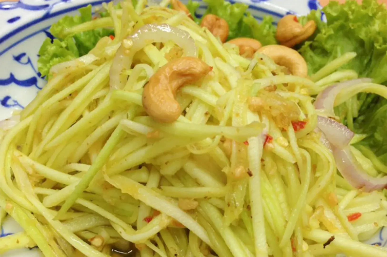 A fresh Thai Green Mango Salad (Yam Mamuang) topped with toasted cashew nuts and sliced red onions.