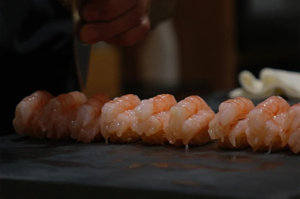 A row of fresh Amaebi (sweet shrimp) nigiri sushi lined up on a traditional dark stone serving board.