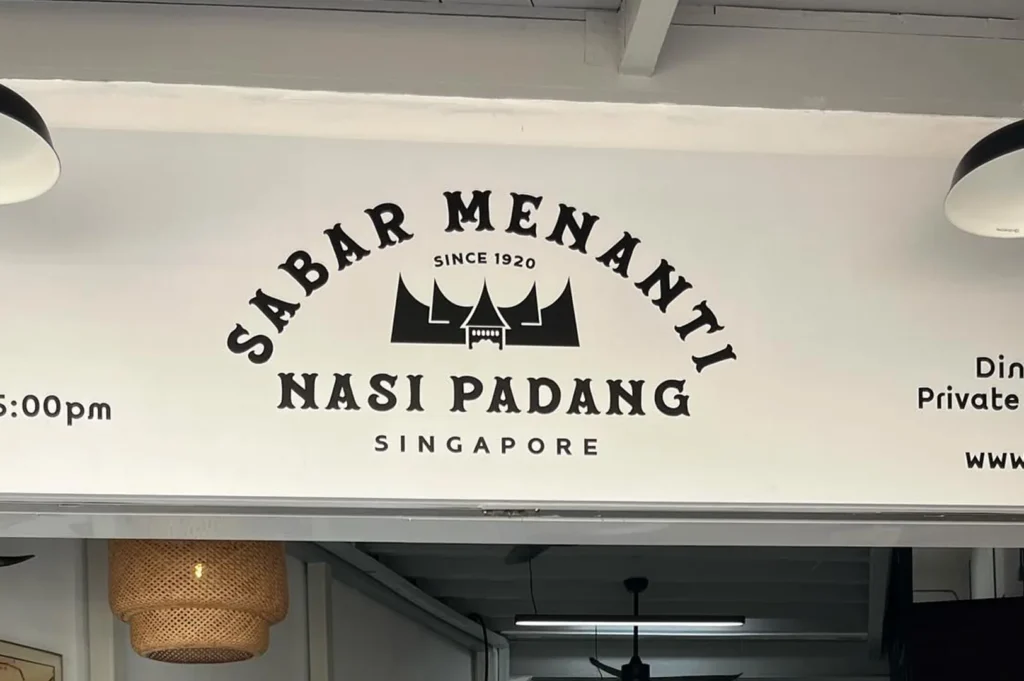 The minimalist black and white storefront sign for Sabar Menanti Nasi Padang in Singapore, established in 1920.