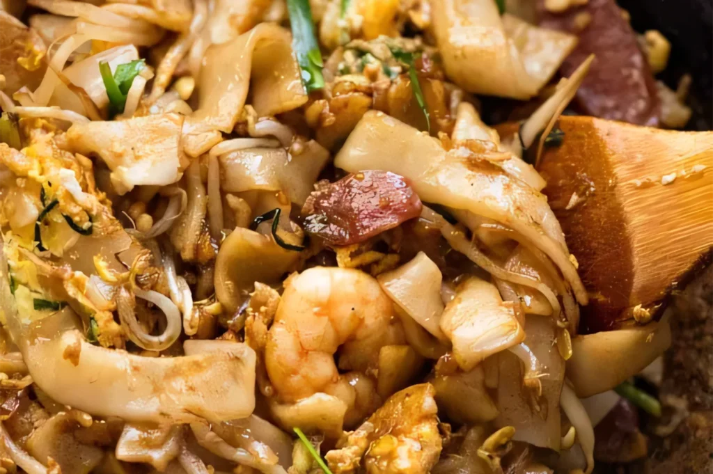 Close-up of Char Kway Teow, featuring stir-fried flat rice noodles with succulent shrimp, Chinese sausage (lap cheong), bean sprouts, and egg.