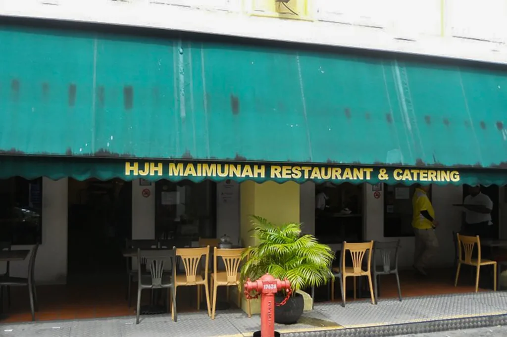 The exterior storefront of the famous Hjh Maimunah Restaurant & Catering with its iconic green awning and outdoor seating.
