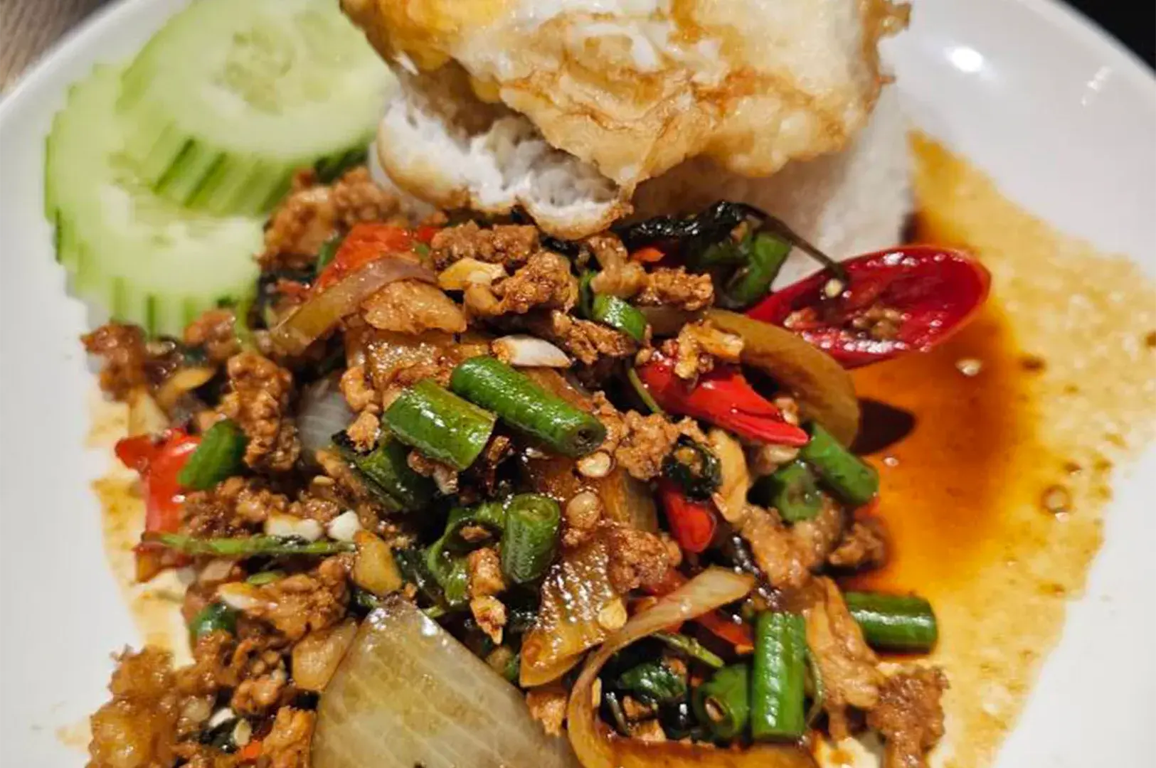 Pad Kra Pao (Thai Basil Pork) served with white rice, sliced cucumbers, and a crispy fried sunny-side-up egg.