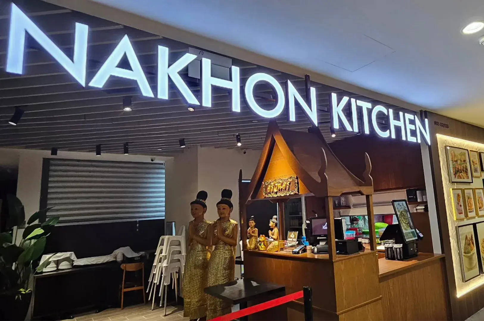 The storefront of Nakhon Kitchen featuring a modern glowing sign and traditional Thai statues at the entrance.