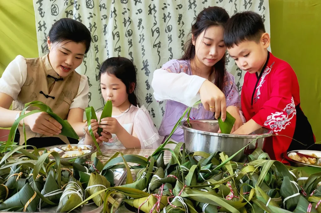 Traditional Chinese family wrapping zongzi dumplings with bamboo leaves during Dragon Boat Festival preparation at home