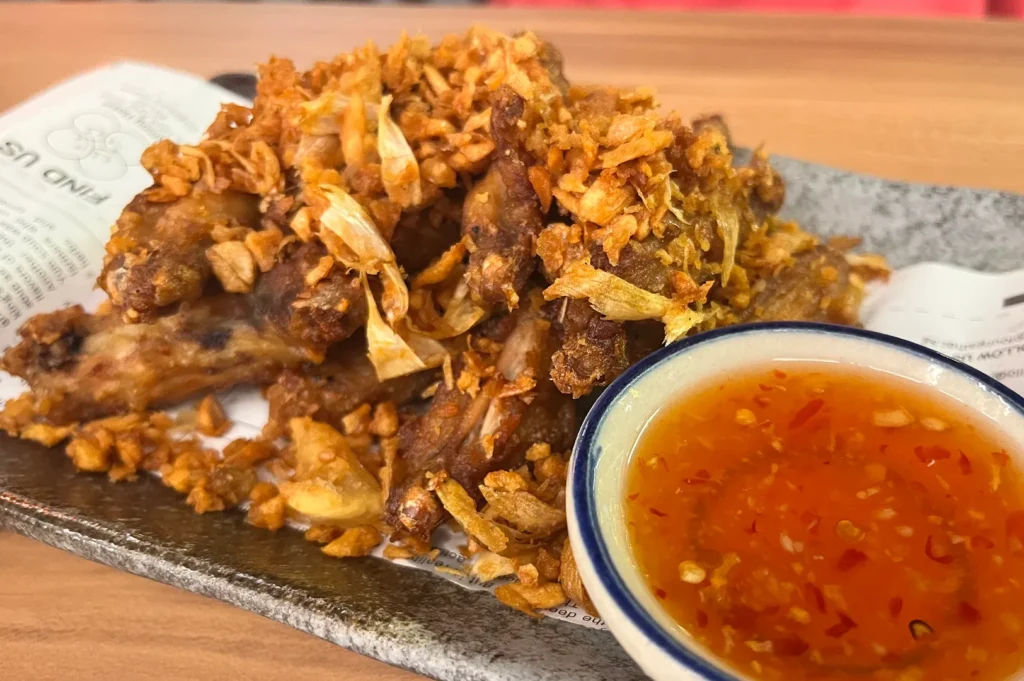 Deep-fried golden brown chicken wings heavily topped with crispy fried garlic, served with a side of sweet chili dipping sauce.