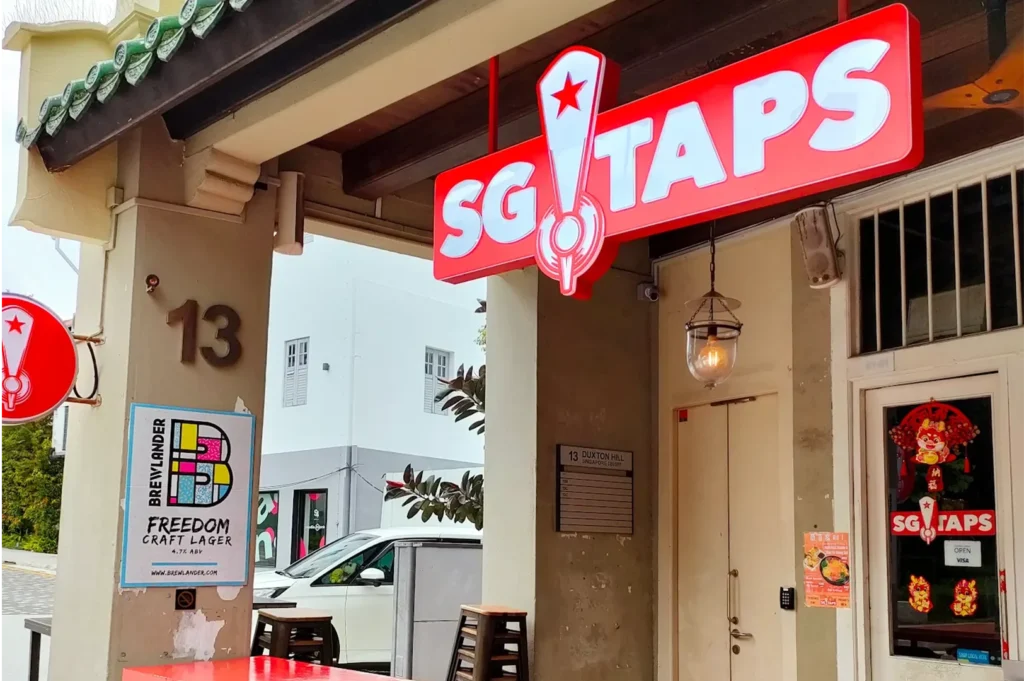 The exterior entrance of SG TAPS craft beer bar at 13 Duxton Hill, Singapore, featuring red signage and outdoor seating.