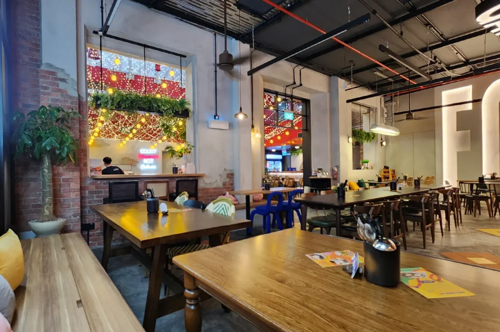 The interior of an industrial-style restaurant featuring wooden tables, exposed brick walls, and warm decorative lighting.