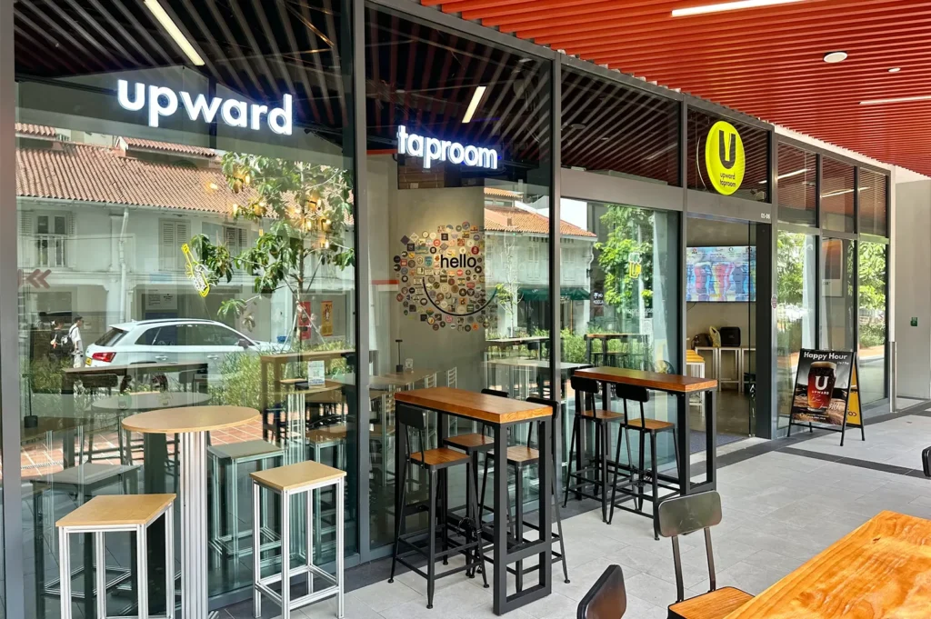 A bright, modern storefront of Upward Taproom with glass walls, high wooden tables, and industrial bar stools.