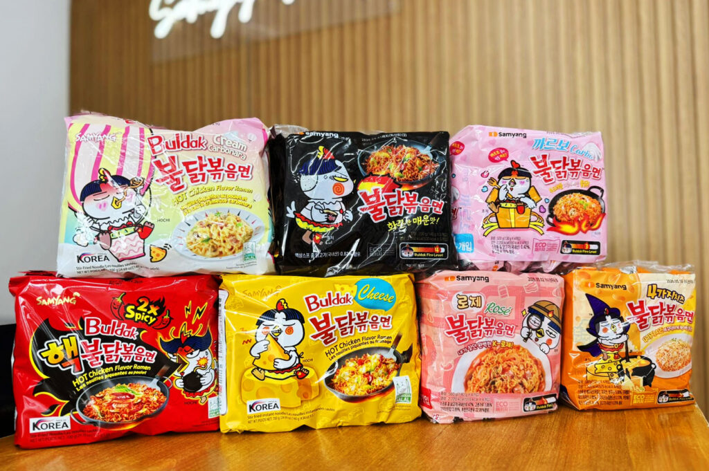 Different Samyang Buldak instant noodle flavours including carbonara, cheese, rose, and spicy Korean ramen varieties displayed on a table