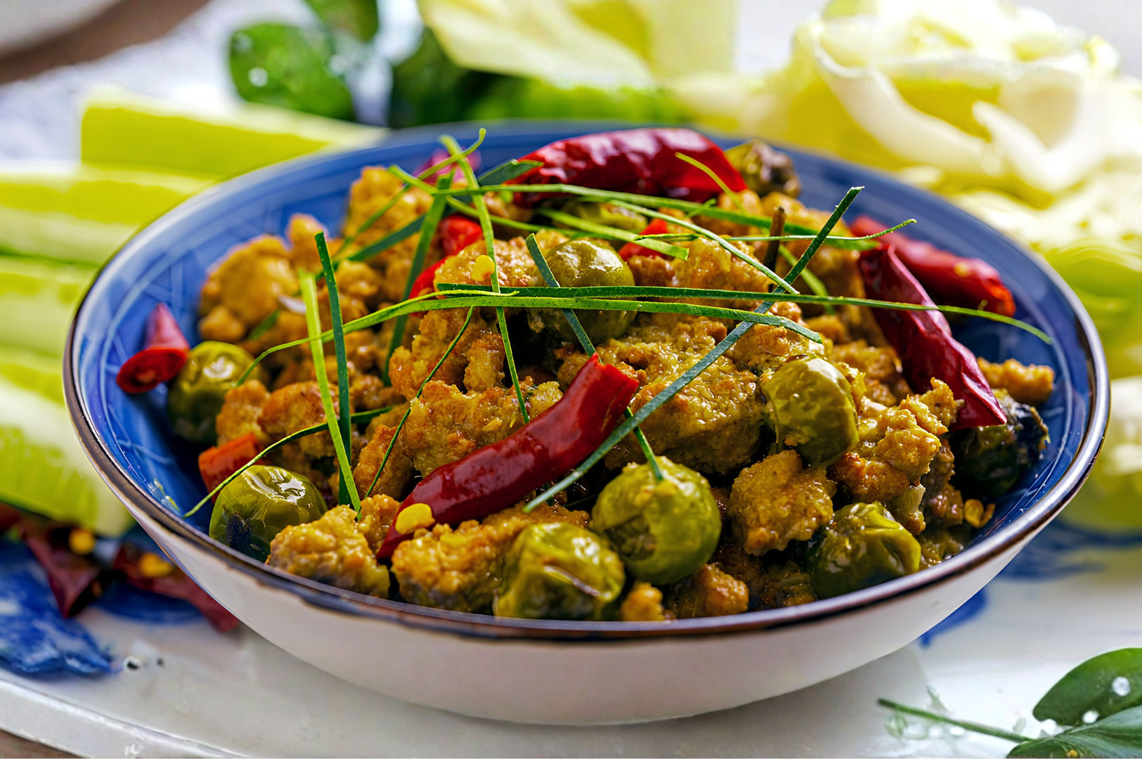 Traditional Cambodian prahok dish with fermented fish paste, Thai eggplants, dried red chillies, and fresh herbs served in a rustic bowl