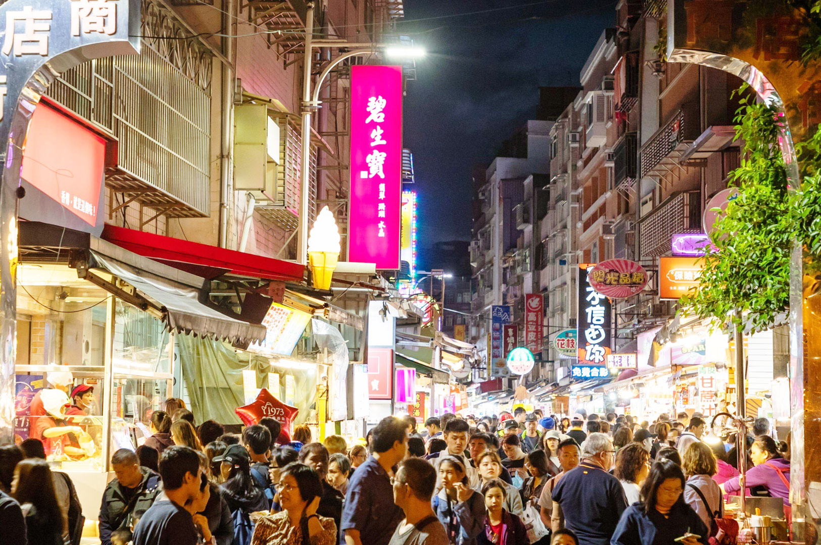 Crowded Taiwan night market street in Tamsui with neon signs, local food stalls, and evening street food culture near the waterfront.