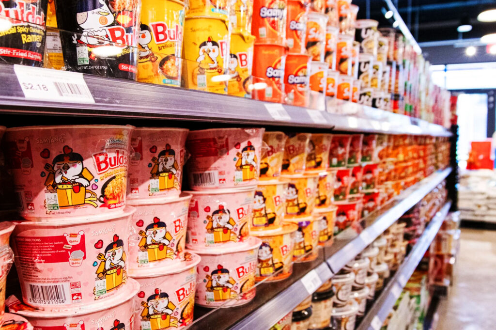 Samyang Buldak instant noodles and Korean ramen cups displayed on supermarket shelves in an Asian grocery store