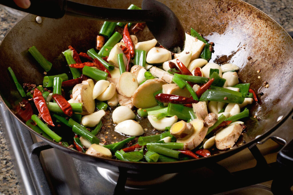 Garlic, ginger, spring onions, and dried chillies sizzling in a wok during preparation of a Chinese eggplant stir fry recipe