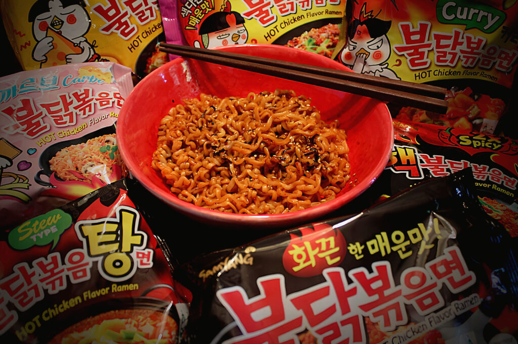 Bowl of Samyang Buldak spicy Korean noodles surrounded by different instant ramen flavours and packaging in a dramatic food setup