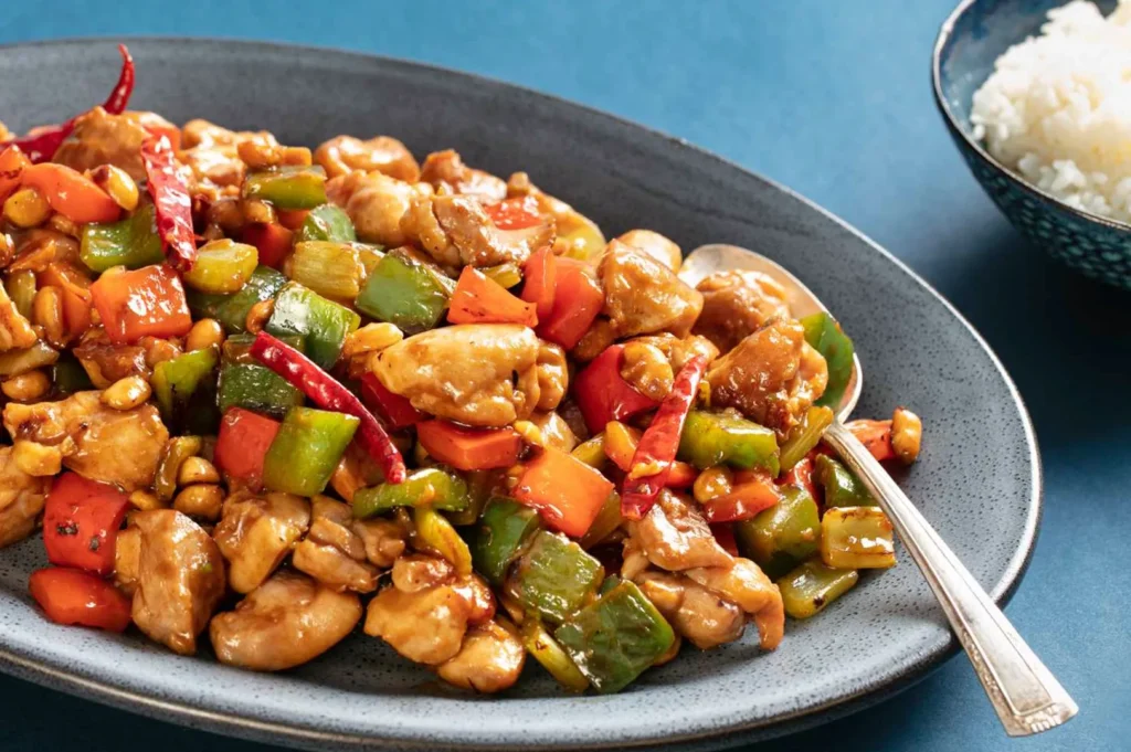 Homemade Kung Pao chicken stir-fry with chicken, peanuts, bell peppers, and dried red chilies served with steamed rice.