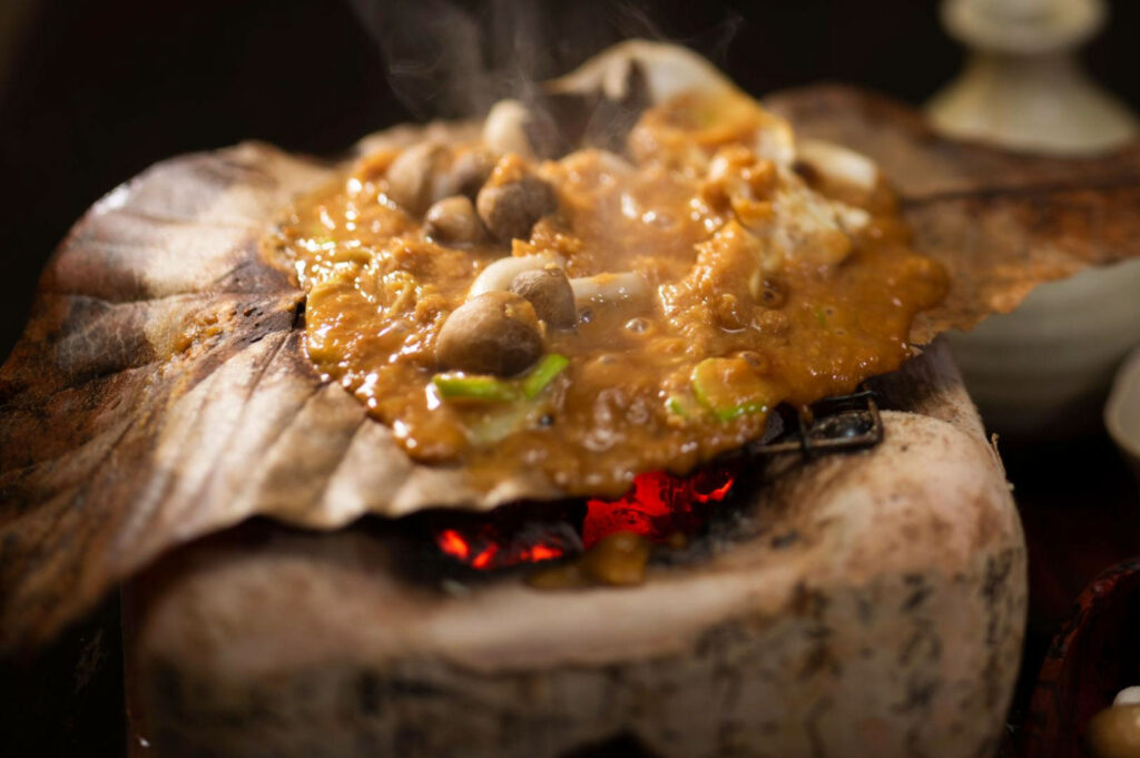 Hoba miso with mushrooms bubbling over magnolia leaf on charcoal grill