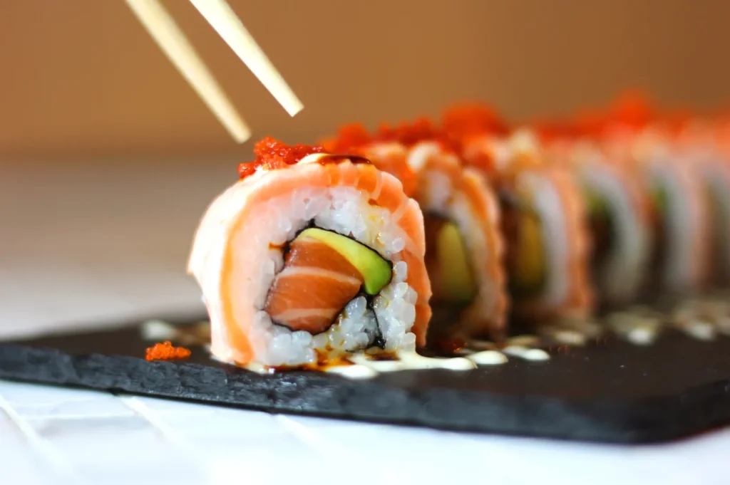 Close-up of salmon sushi roll with avocado and tobiko topped with creamy Japanese sauce