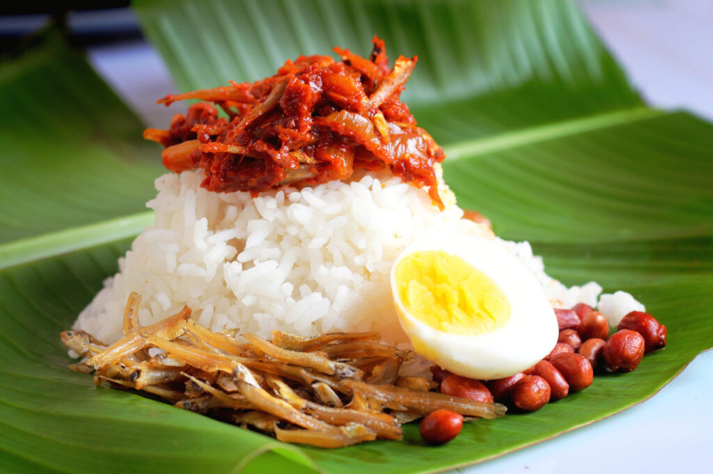 Authentic nasi lemak with sambal, boiled egg, anchovies, peanuts, and coconut rice on a banana leaf.