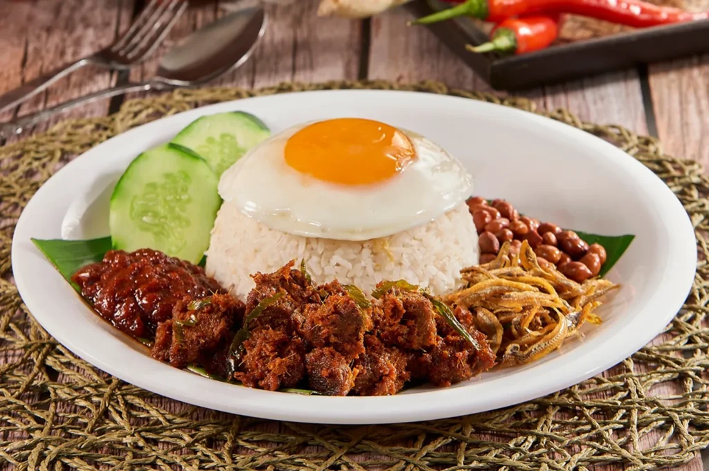 Malaysian nasi lemak with fried egg, sambal, anchovies, peanuts, cucumber, and crispy rendang-style chicken.