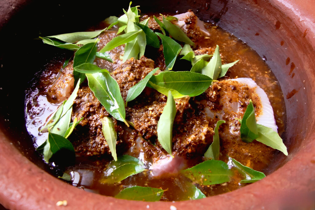 Traditional Sri Lankan fish curry cooking in a clay pot with fresh curry leaves and spiced tuna for Ambul Thiyal preparation.