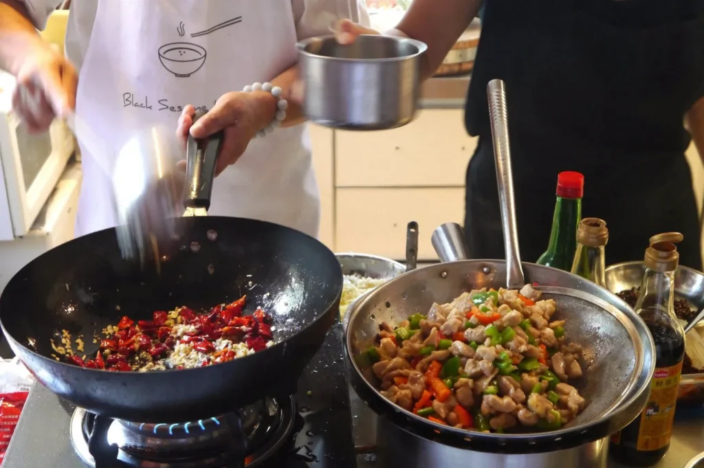 Cooking Kung Pao chicken in a wok with fresh vegetables, dried chilies, garlic, and traditional Chinese seasonings.