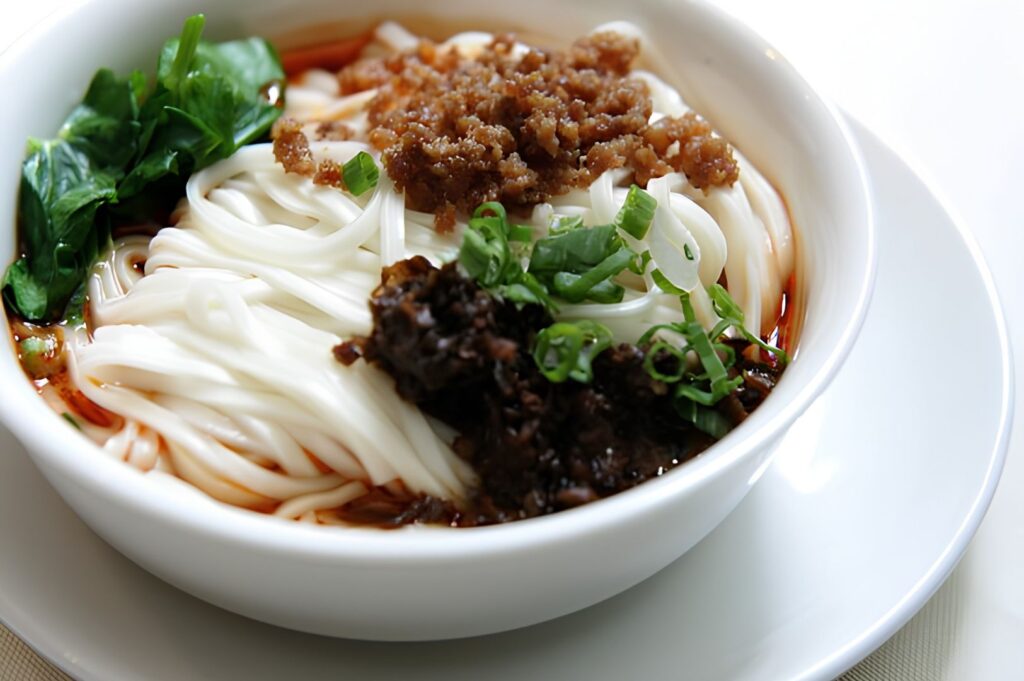 Handmade Chinese noodles with minced pork, chili oil, and fresh greens served in white ceramic bowl at upscale Sichuan restaurant Singapore