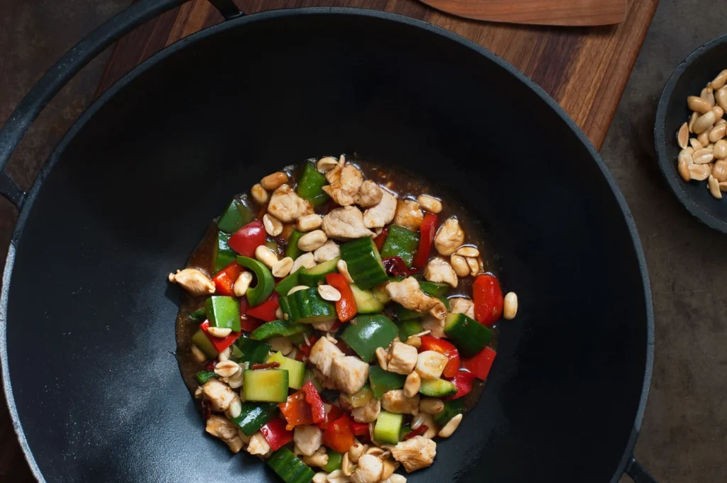 Kung Pao chicken cooking in a wok with bell peppers, peanuts, and traditional Sichuan seasonings.