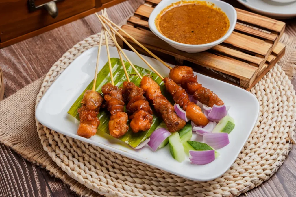 Malaysian chicken satay skewers with peanut sauce, cucumber, and red onions.
