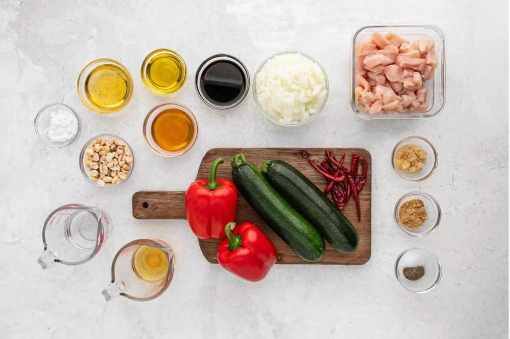 Kung Pao chicken ingredients with diced chicken, peanuts, dried chilies, bell peppers, zucchini, soy sauce, and seasonings for a homemade Sichuan recipe.
