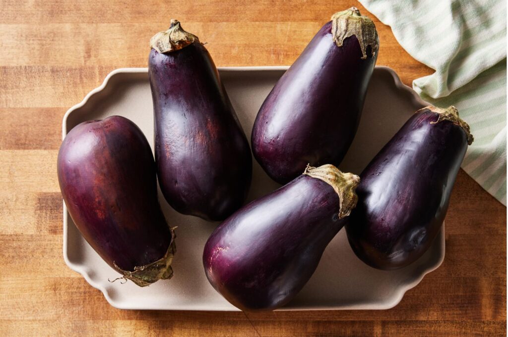 Fresh purple Chinese eggplants arranged on ceramic tray for Sichuan cooking ingredients and Asian vegetable preparation photography