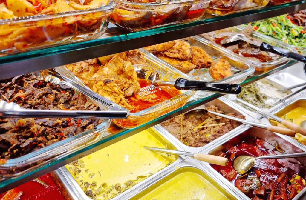Selection of Malaysian nasi campur, curries, and home-style dishes displayed in a vibrant hawker-style food counter.