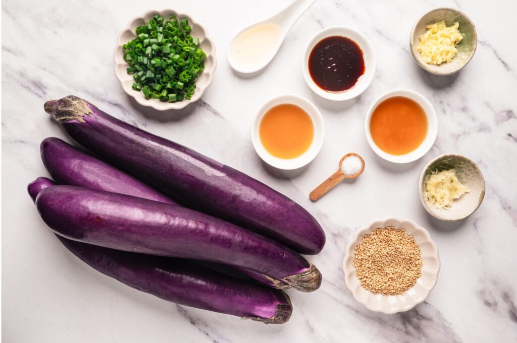 Chinese eggplant ingredients flat lay with sesame seeds, garlic, sauces, and spring onions prepared for Sichuan stir-fry recipe cooking scene