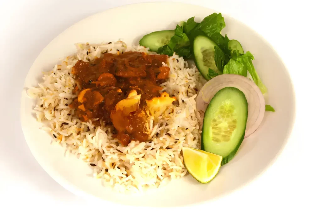 Chicken curry over fluffy jeera rice with fresh cucumber salad and lime