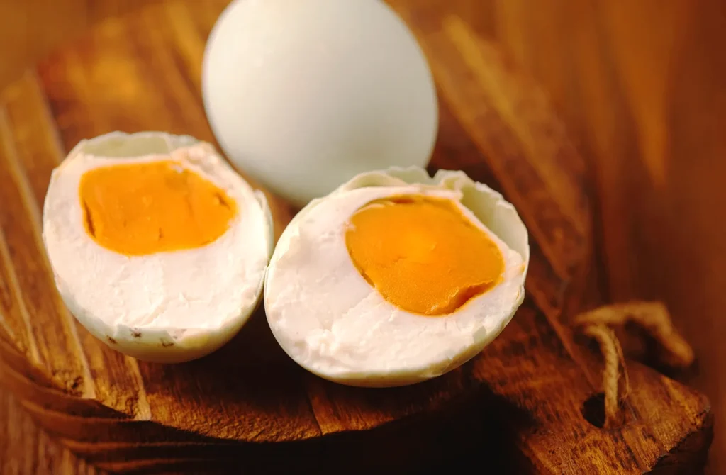 Salted duck egg halves with rich orange yolks on a wooden board, showcasing the traditional ingredient behind Singapore salted egg dishes