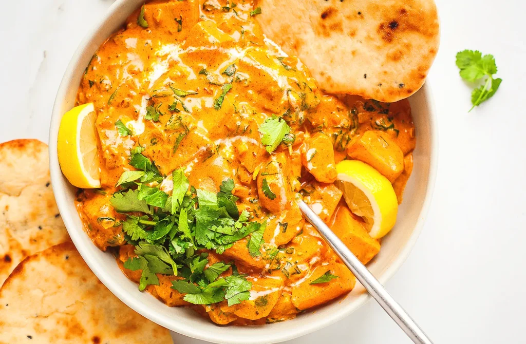 Creamy Indian potato curry with naan bread and fresh cilantro garnish in a serving bowl