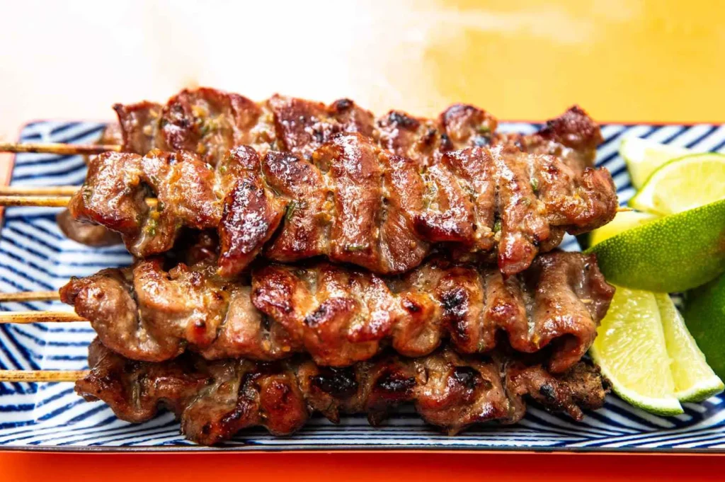 Grilled moo ping pork skewers with smoky char, bamboo sticks, and fresh lime wedges