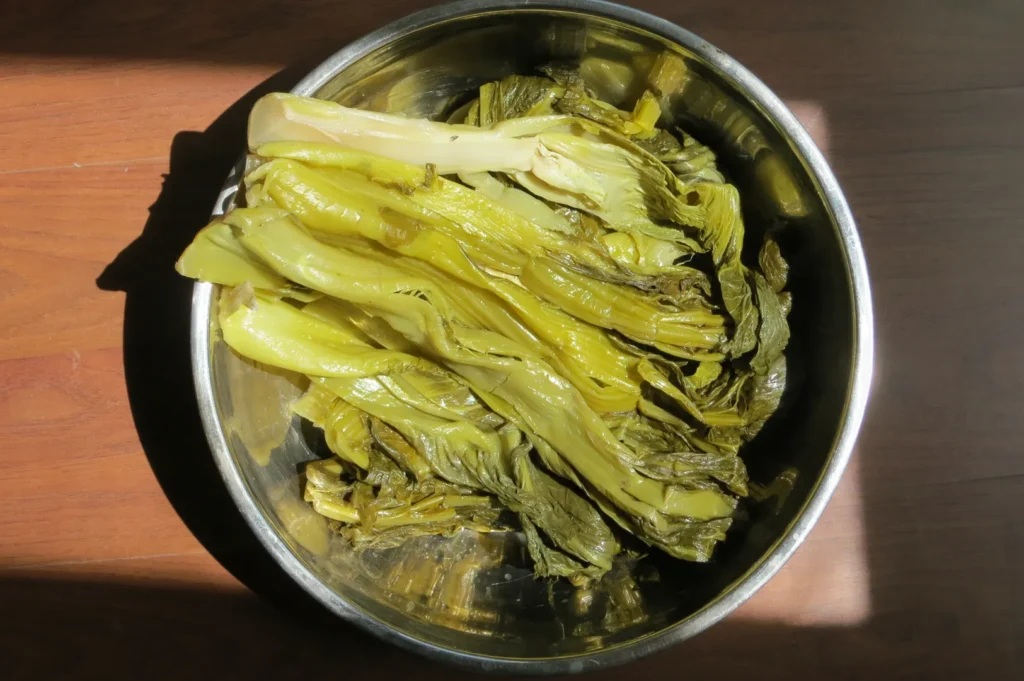 Homemade pickled mustard greens in a glass jar with chopsticks for Asian soups