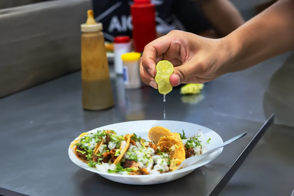 Close-up of fresh calamansi juice being squeezed over street food tacos, highlighting the bright citrus garnish and authentic dining experience.