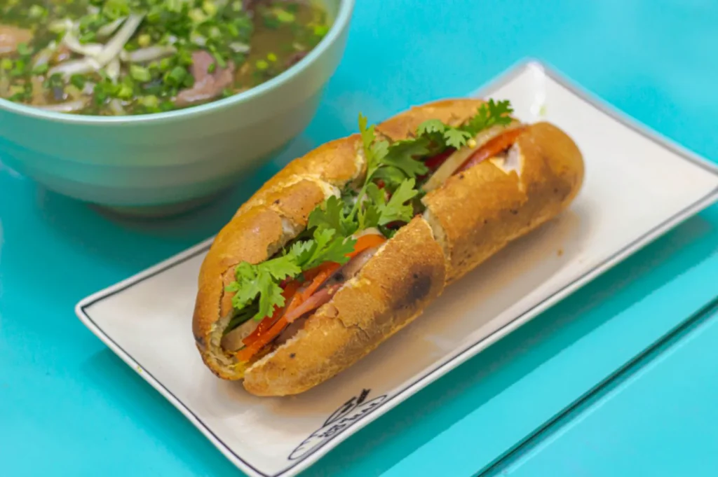 Authentic Vietnamese bánh mì sandwich with fresh herbs served alongside a bowl of traditional beef pho at Co Hai Banh Mi Singapore.