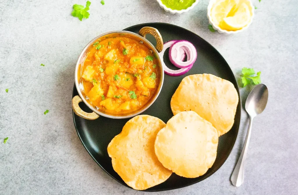Traditional potato curry served with fluffy puri bread and fresh onion on a black plate