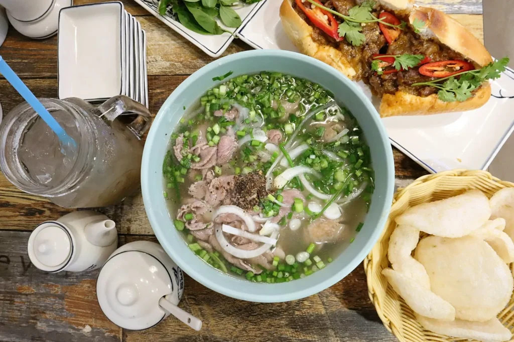 Traditional Vietnamese beef pho with fresh herbs, crispy prawn crackers, and signature bánh mì at Co Hai Banh Mi Singapore.