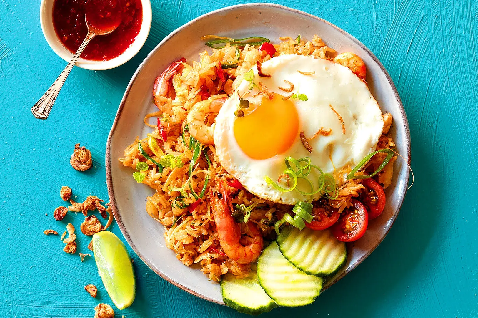 Indonesian nasi goreng with shrimp, fried egg, vegetables, cucumber, and lime garnish