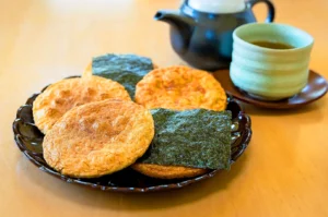 Traditional Japanese senbei rice crackers served with green tea in Kyoto, featuring soy-glazed and nori-wrapped handmade rice crackers on a ceramic plate.