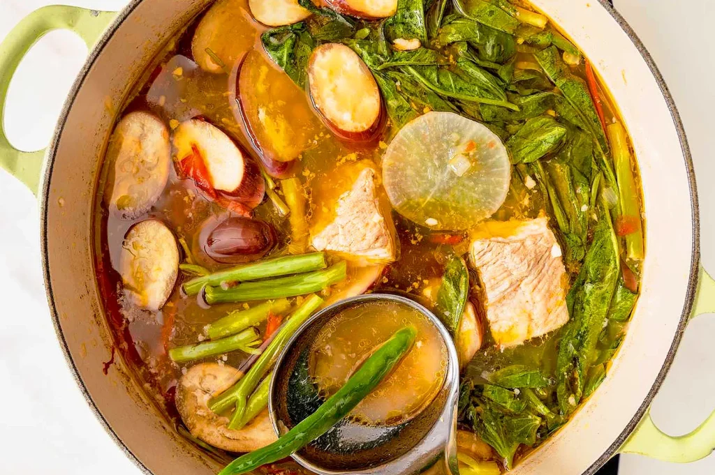 Traditional Filipino sinigang in a cooking pot with pork, kangkong, eggplant, long beans, radish, and tamarind broth.
