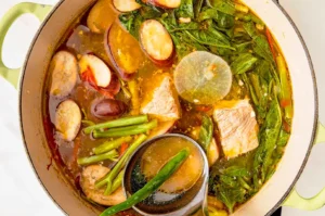 Traditional Filipino sinigang in a cooking pot with pork, kangkong, eggplant, long beans, radish, and tamarind broth.