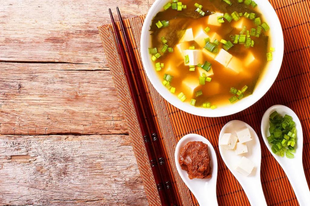 Traditional Japanese miso soup with tofu and green onions served with chopsticks and condiments