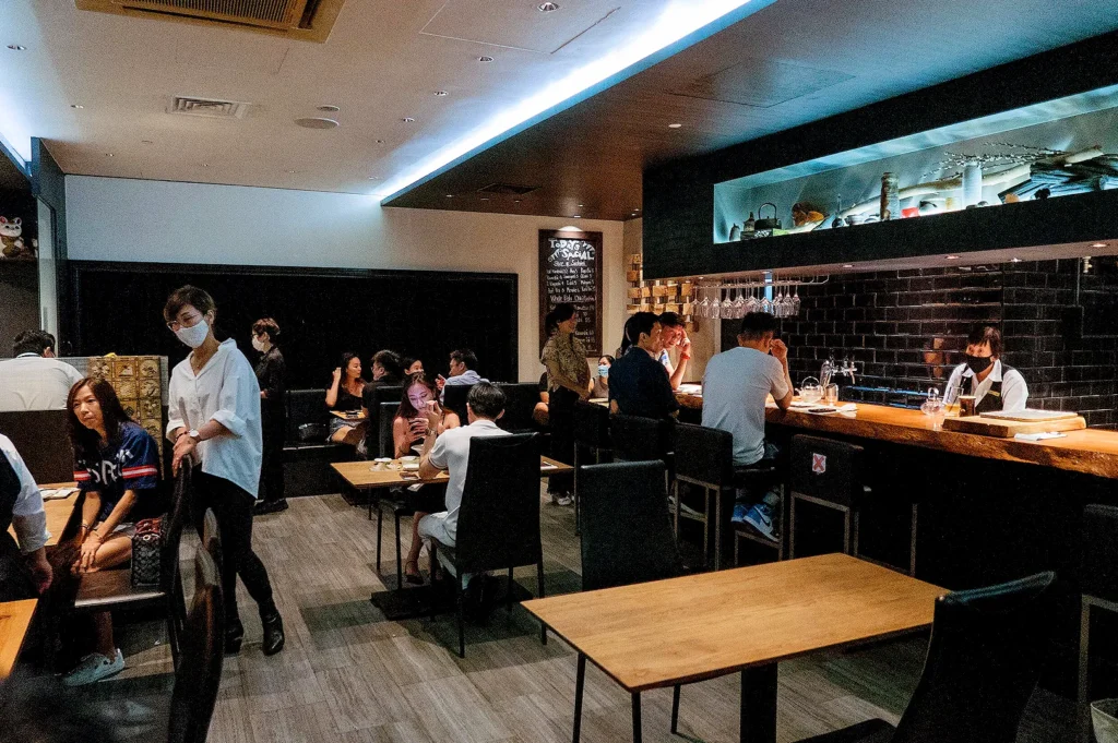 Busy Kazu Sumiyaki Restaurant interior with diners, wooden tables, counter seating and Japanese-style decor in Singapore