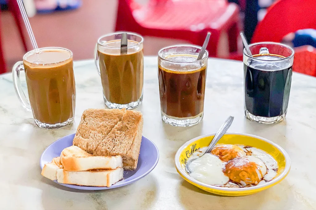 Traditional Singapore kopitiam breakfast with cups of kopi, black coffee, kaya toast, and soft-boiled eggs